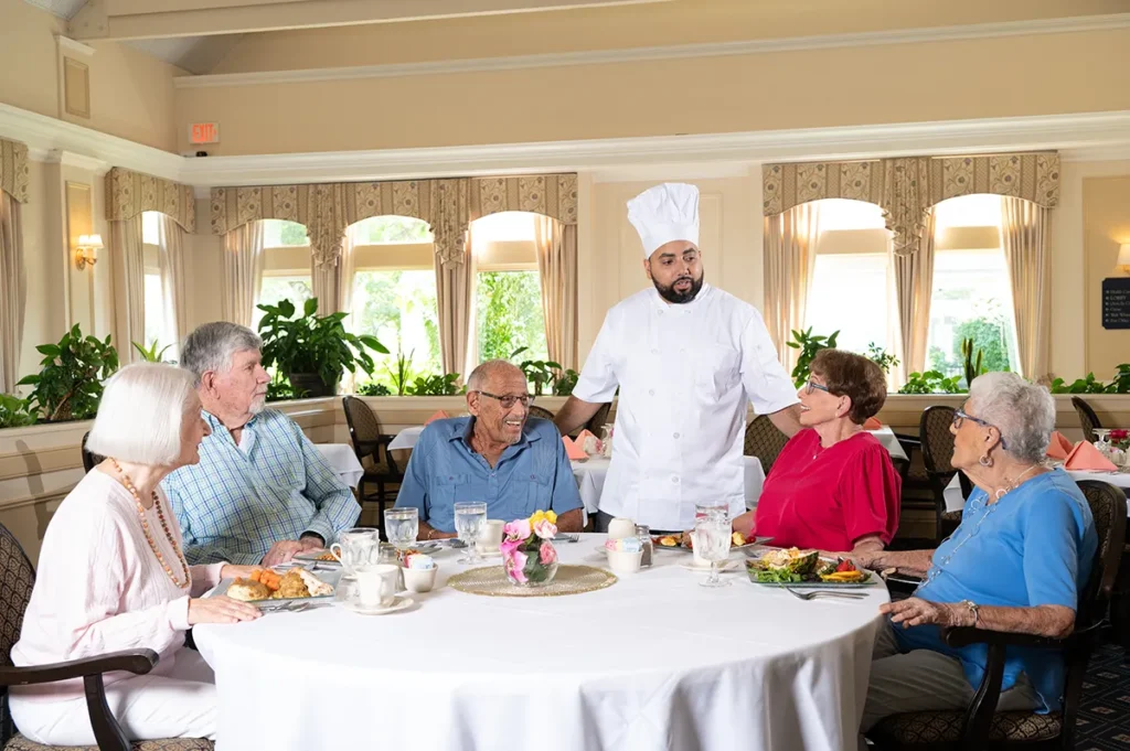 grow of men and women in the dining room being visited by the chef