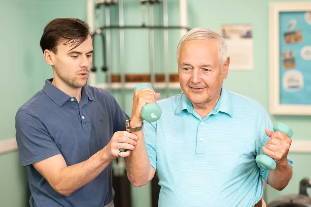 older gentleman lifting hand weights with a physical therapist