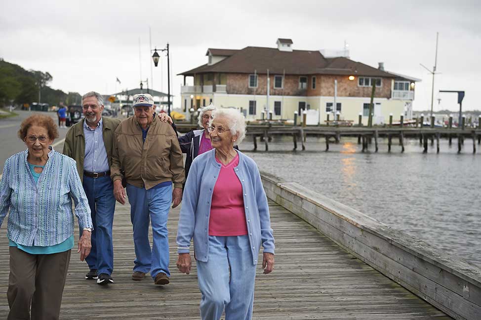 group of men and women walking along the boardwalk at the ocean