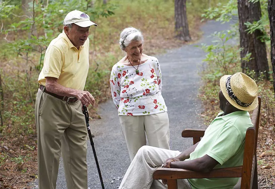 a couple walking outdoors stopping to talk to a gentleman on a bench